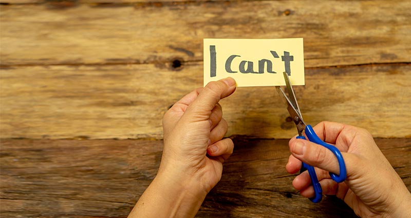 person cutting paper that says "I can't" 