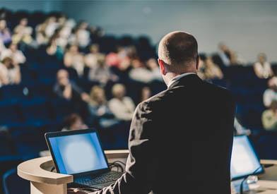 Man speaking at a podium in front of people with hands up